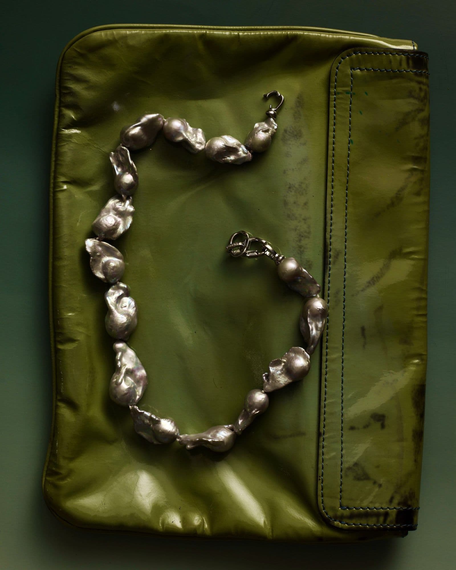 Silver baroque pearl necklace and earring arranged on an olive green leather pouch, shot from above.
